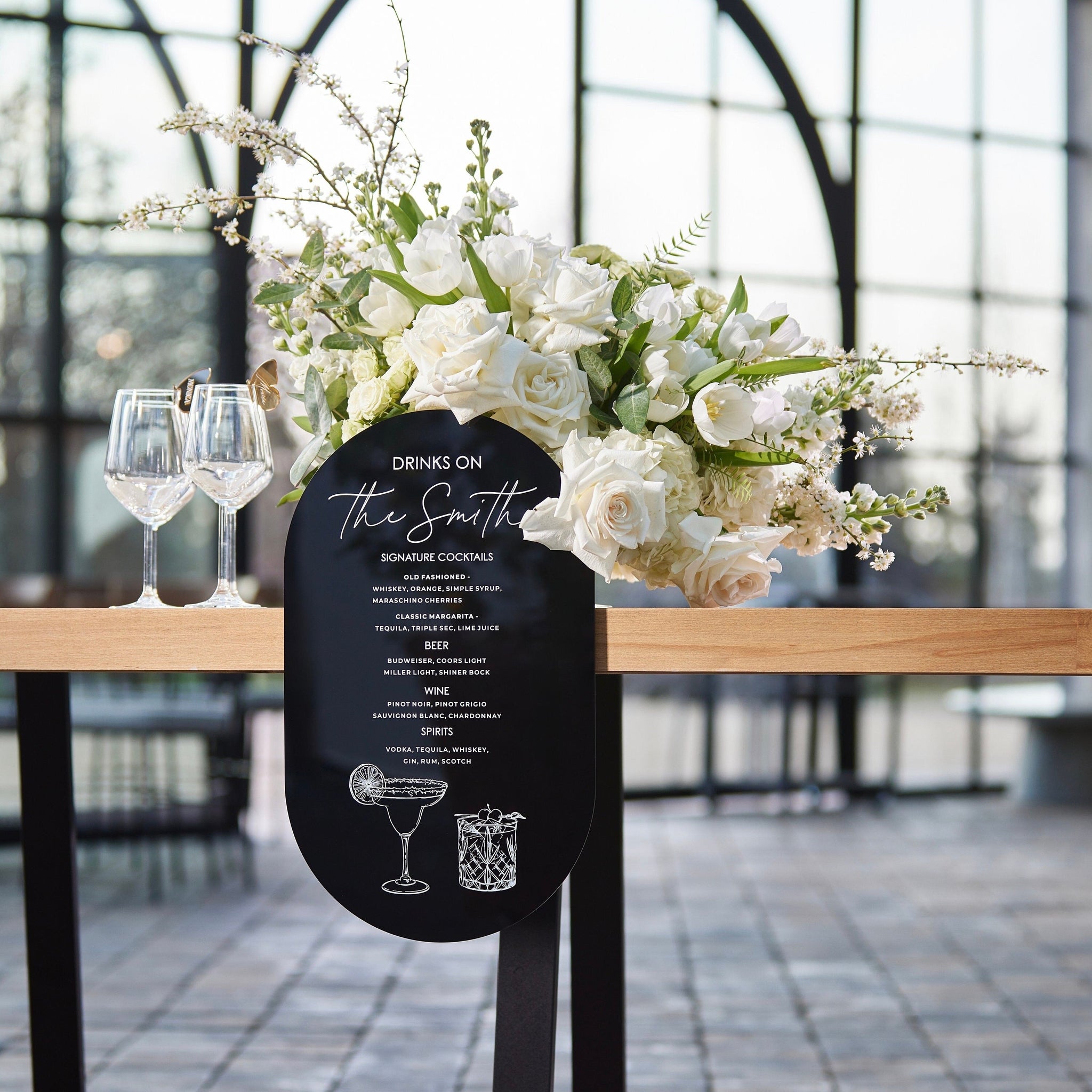 Black acrylic wedding bar sign with white text and cocktail illustrations for signature drinks menu