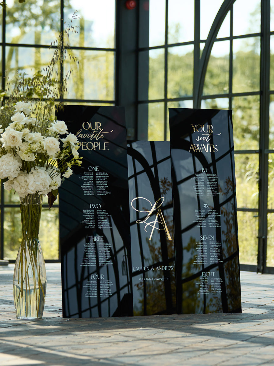 Black acrylic wedding seating chart with white text and 3D gold mirror for reception table assignments