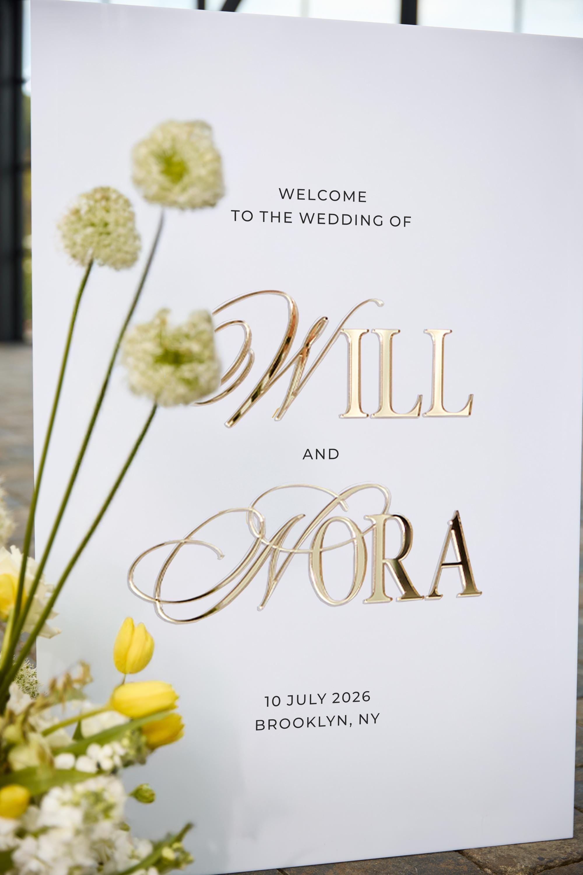 Close-up of white acrylic welcome sign showing 3D raised gold mirror names
