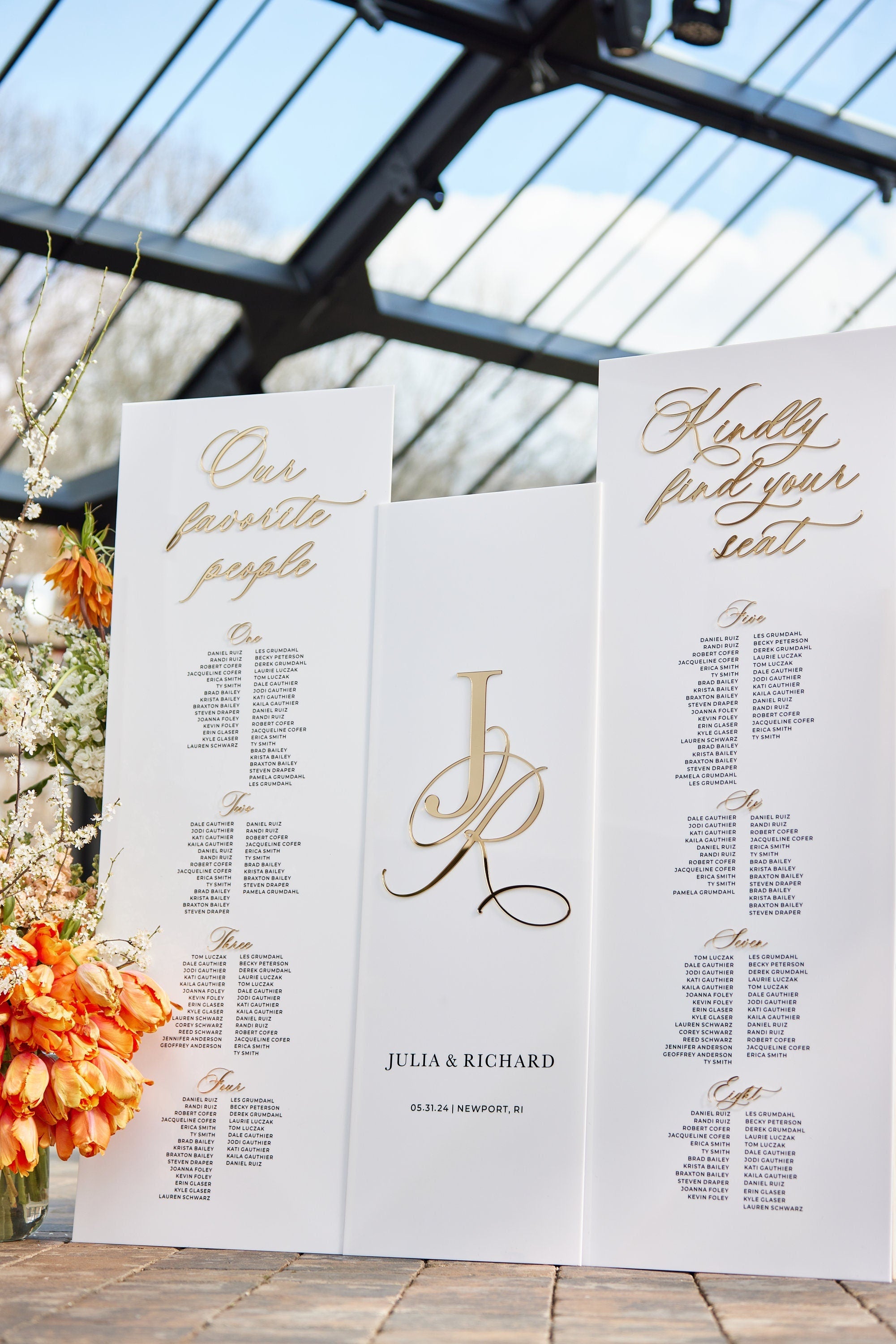 Large white acrylic seating chart with 3D gold mirror headers and guest list layout
