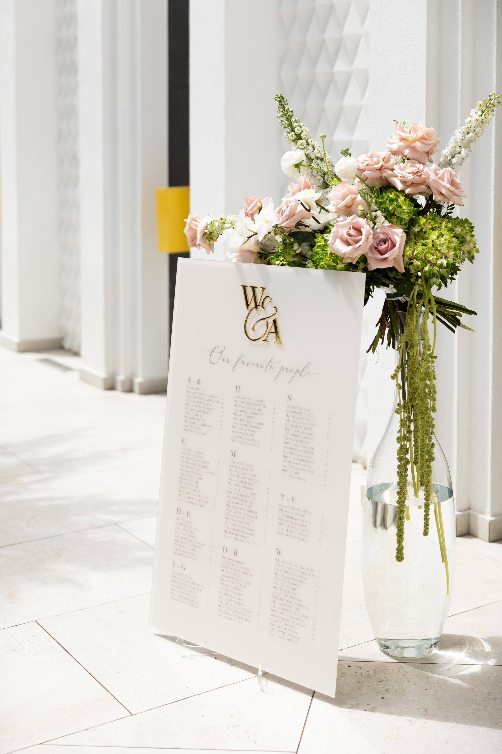 Beige acrylic wedding seating chart with elegant 3D gold mirror monogram
