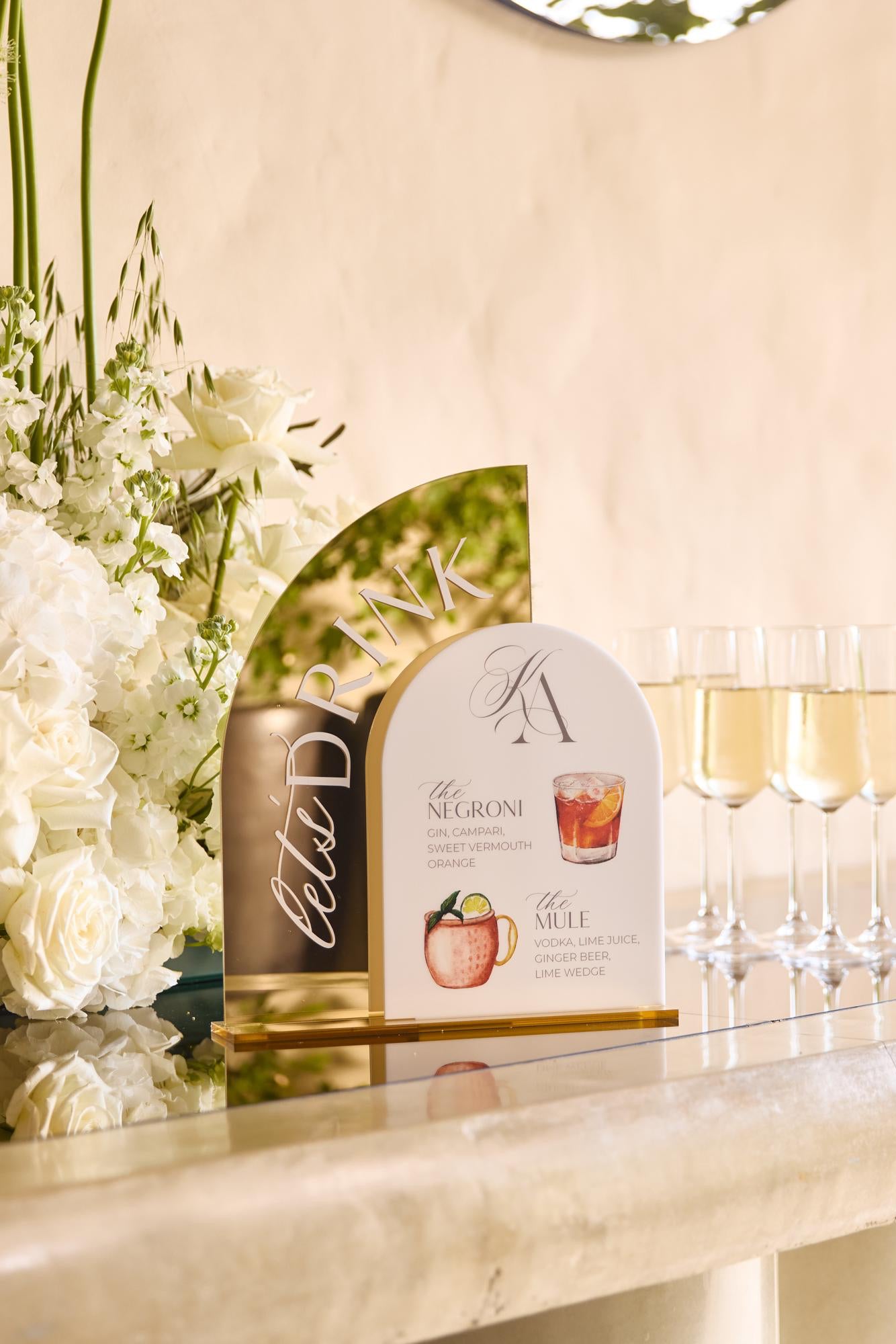 Gold mirror acrylic bar sign on gold stand displaying wedding signature drinks menu
