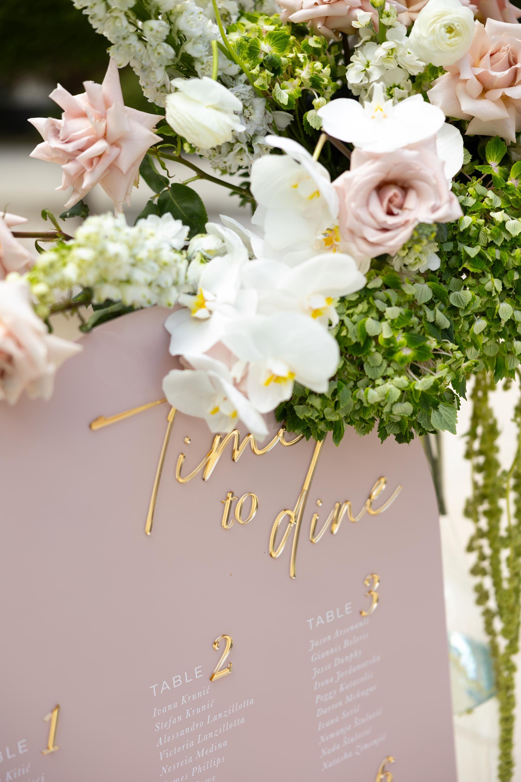 Wedding table assignment sign in pink acrylic with gold mirror text
