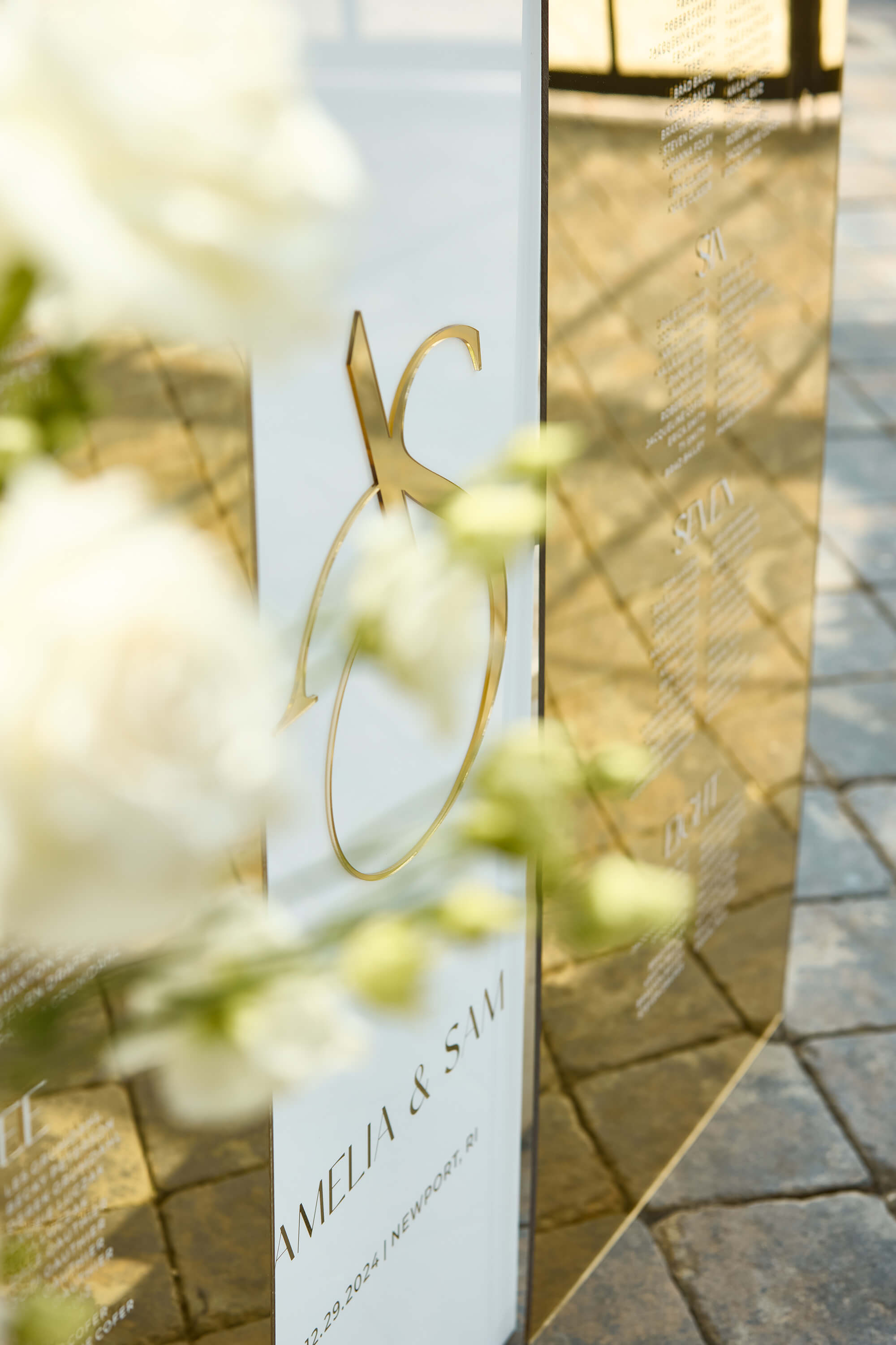 Close up detail of raised 3D gold mirror initials on a white acrylic wedding welcome sign.