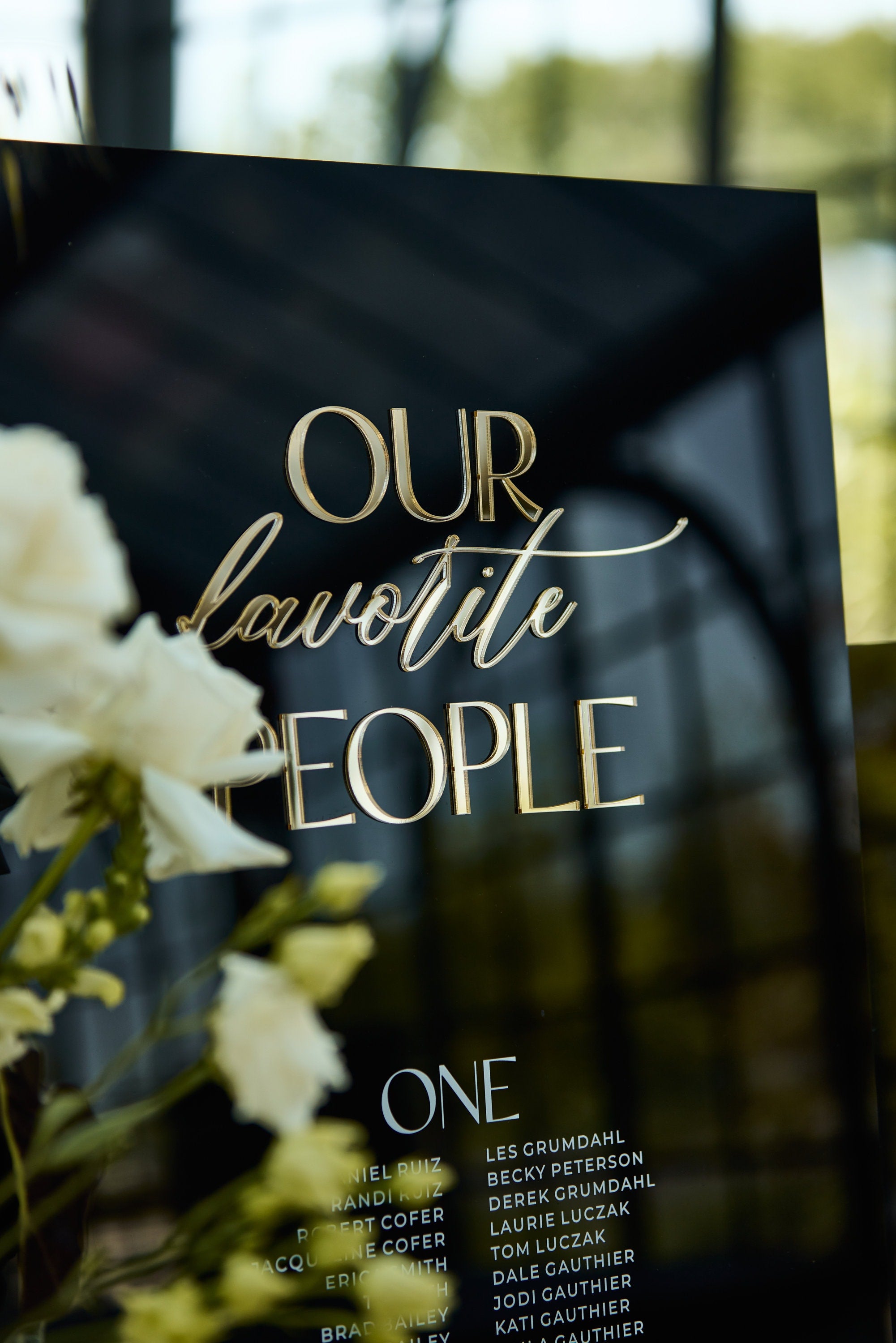 Black acrylic wedding seating chart displaying guest list by table number
