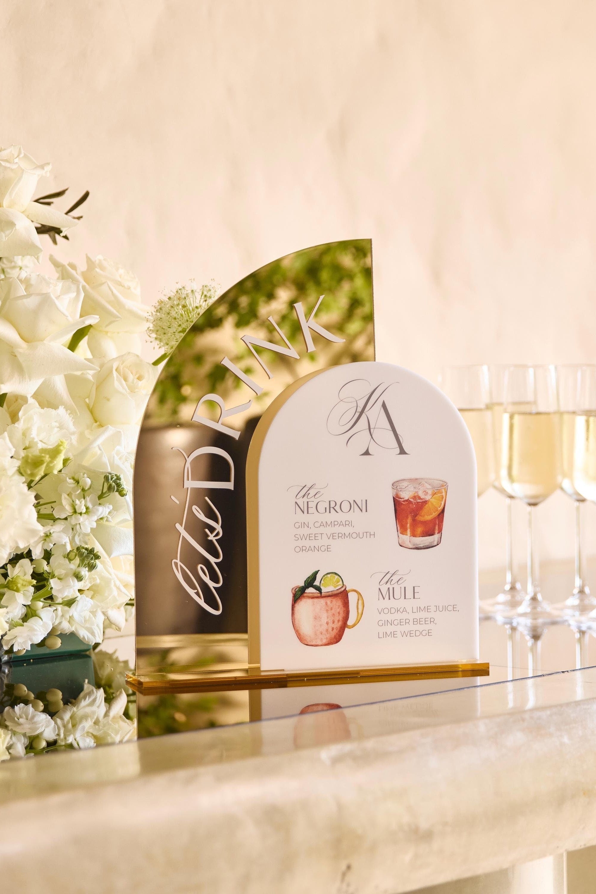 Gold mirror acrylic bar sign with white background displaying signature cocktail menu for wedding reception
