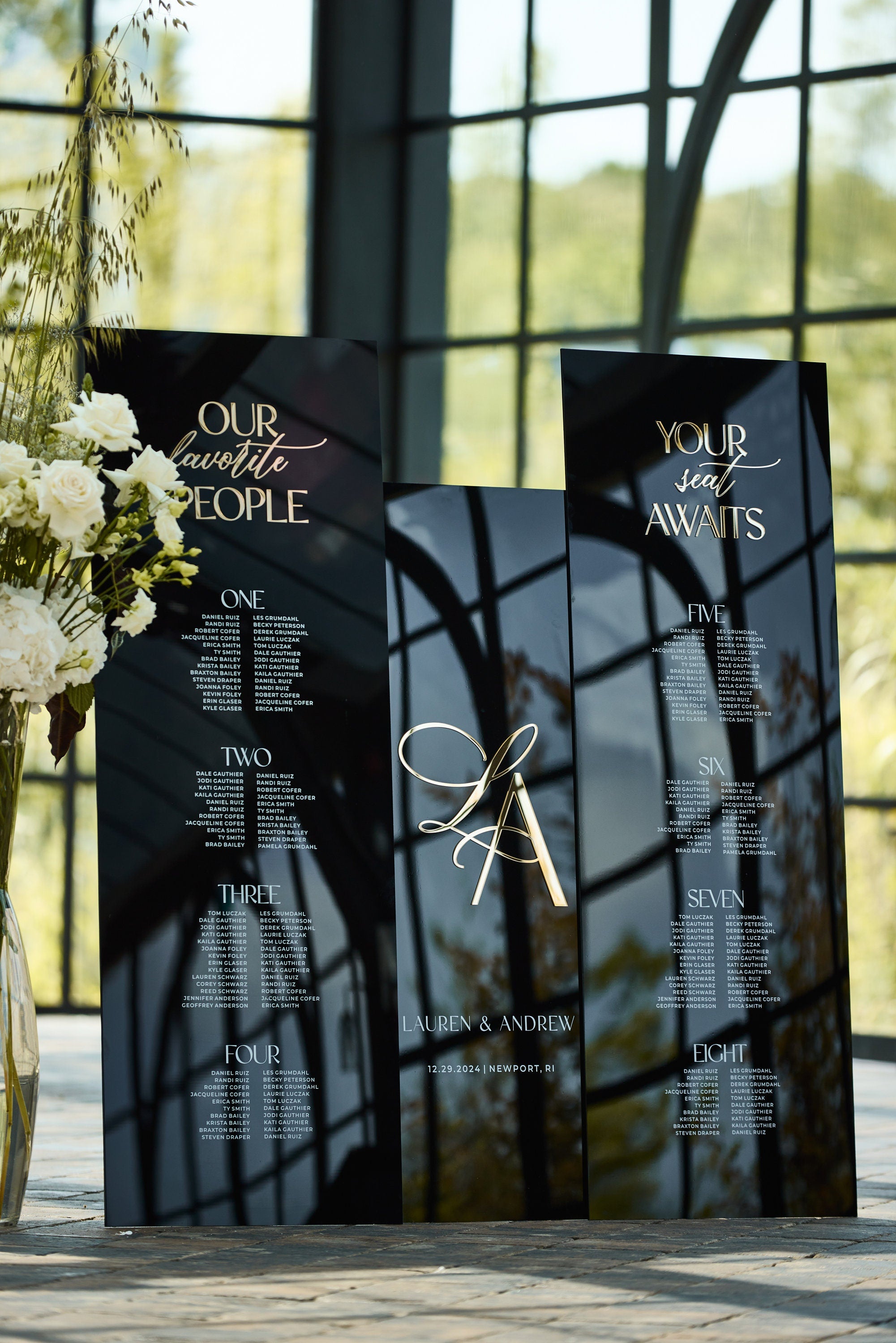 Black acrylic seating plan with gold mirror text and table assignments
