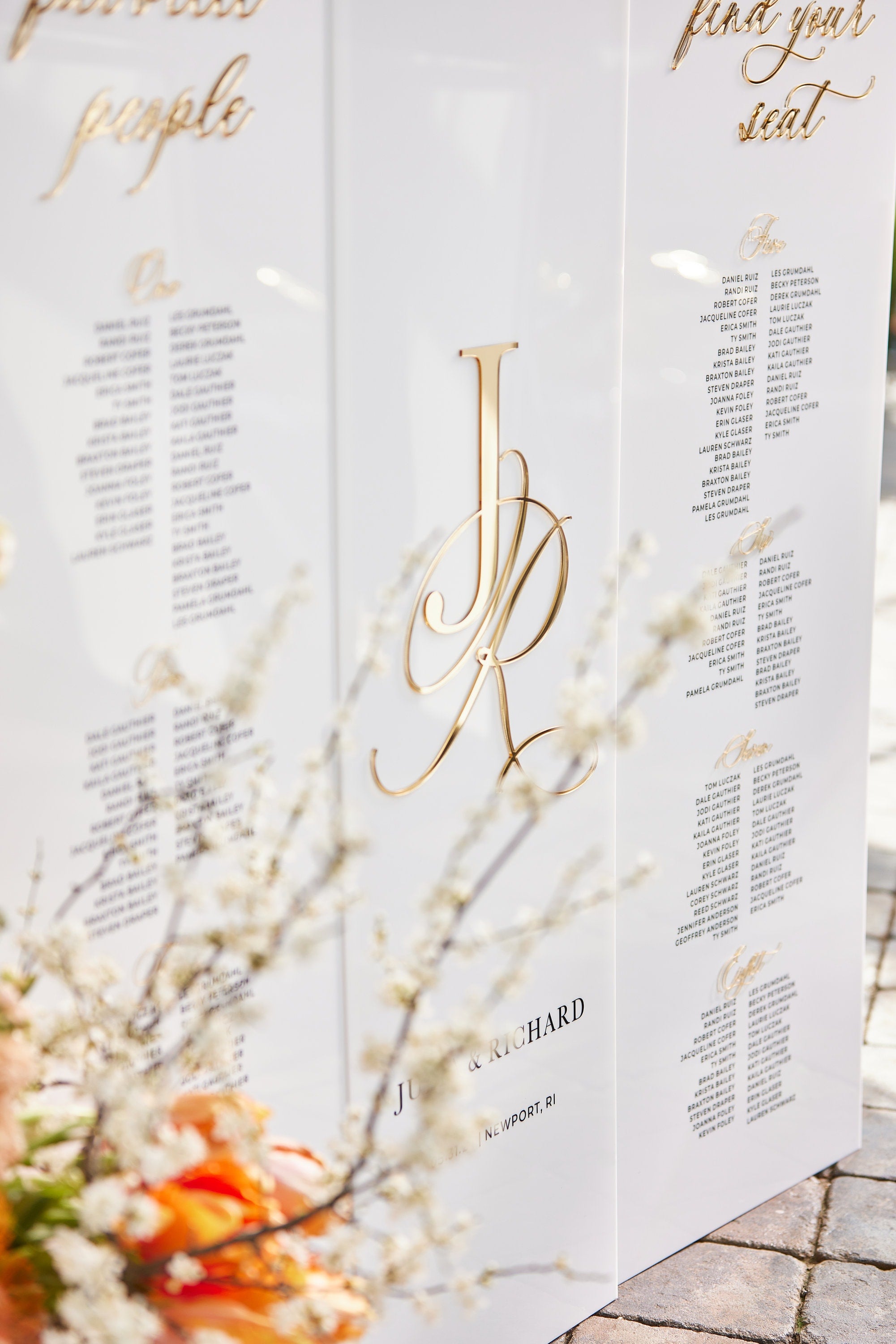 Close-up of 3D gold mirror lettering on white acrylic seating chart showing guest names and table numbers
