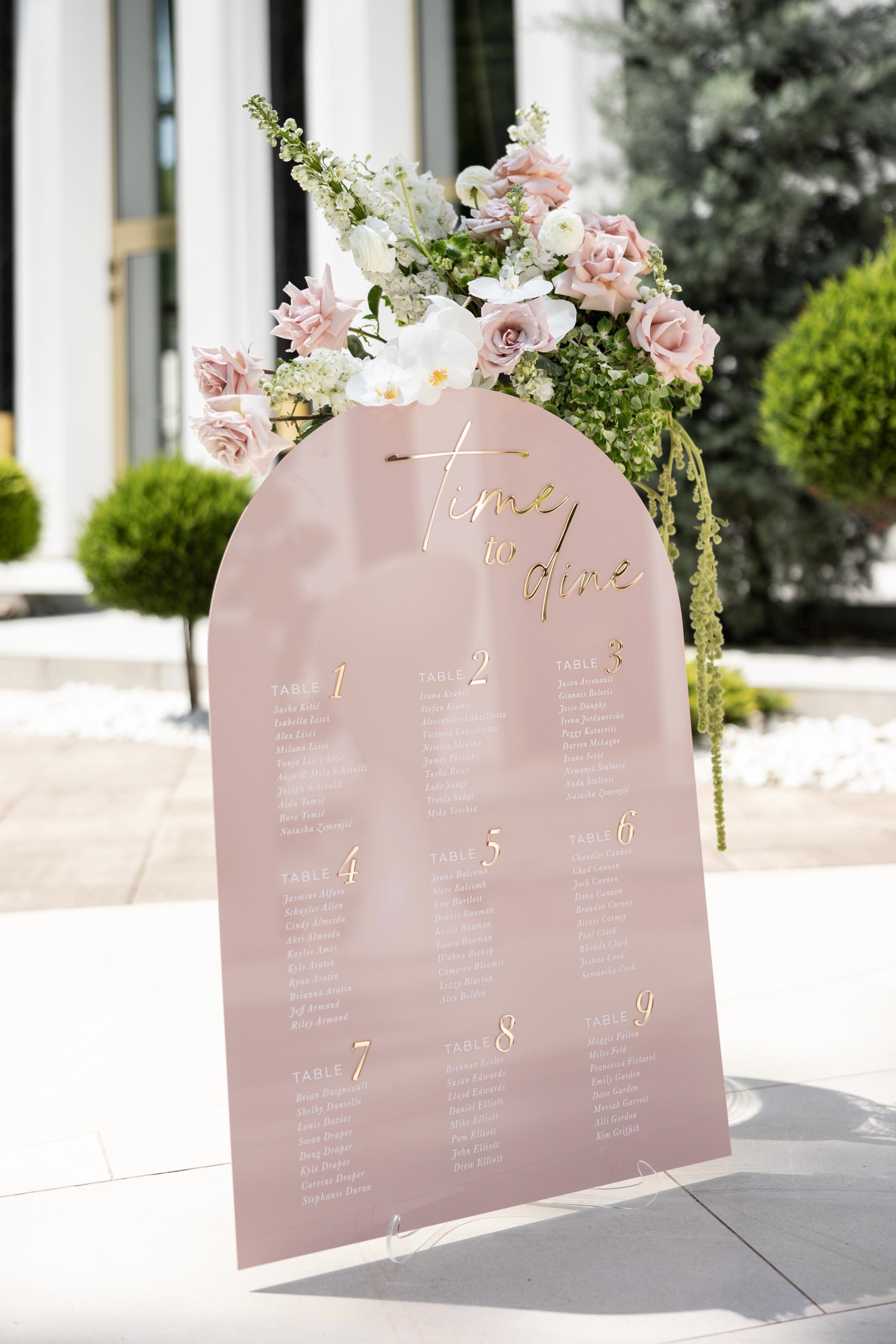 Pink wedding seating chart with gold lettering and guest table assignments
