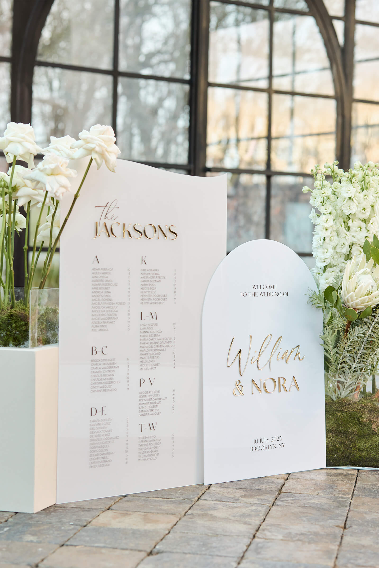 Detail of beige acrylic seating chart with 3D gold mirror header, showing organized guest list columns.