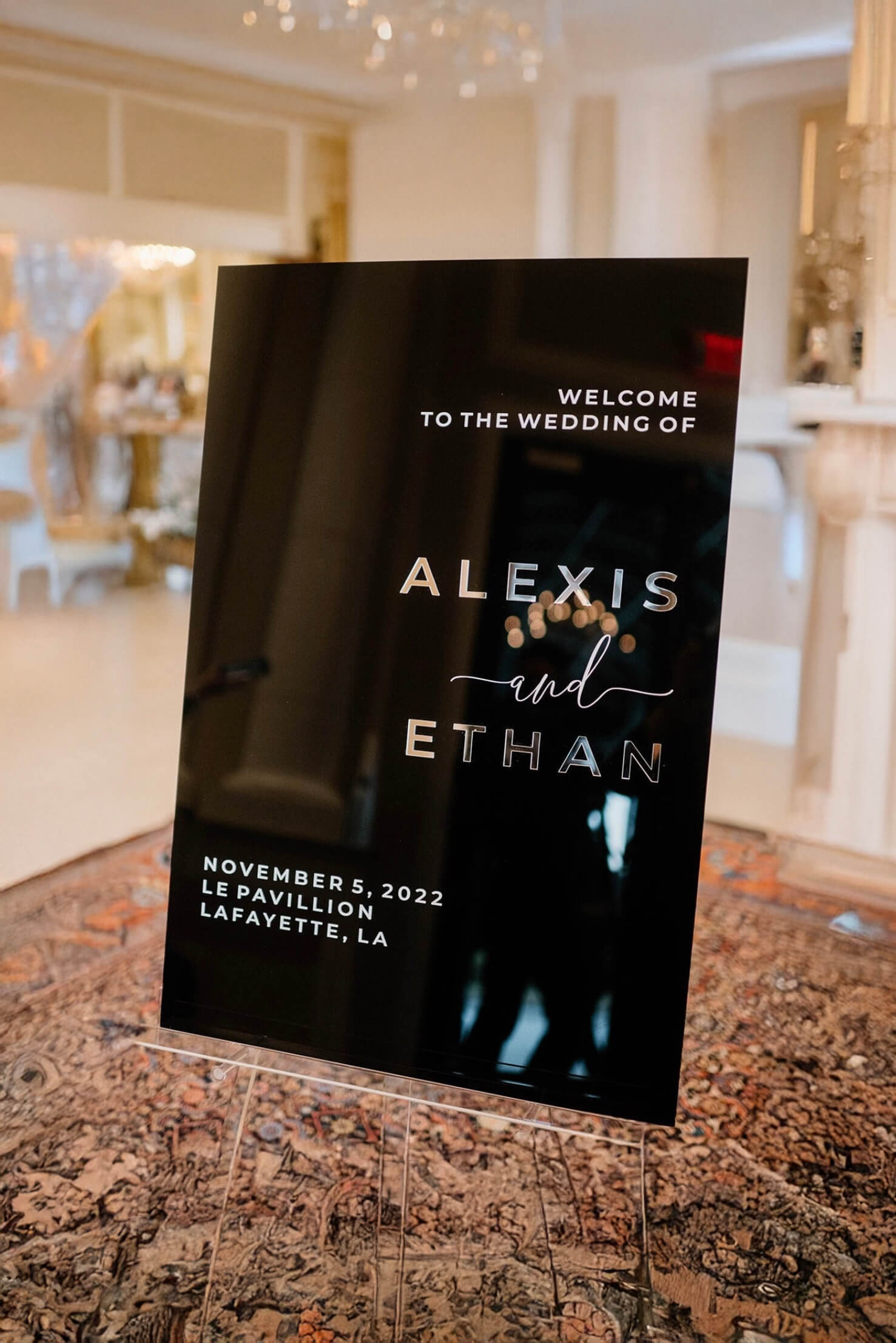 Modern black tie wedding entrance decor featuring a black acrylic welcome sign on an easel.