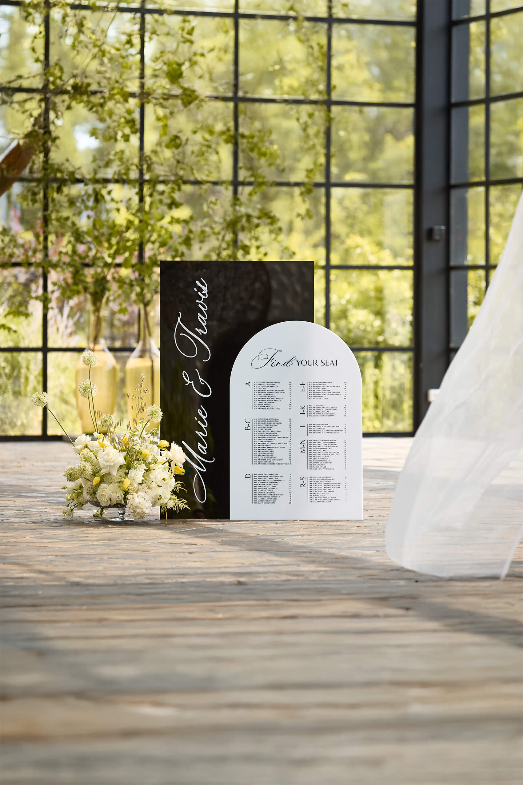 Modern black and white acrylic wedding seating chart featuring 3D raised names and organized guest list columns.