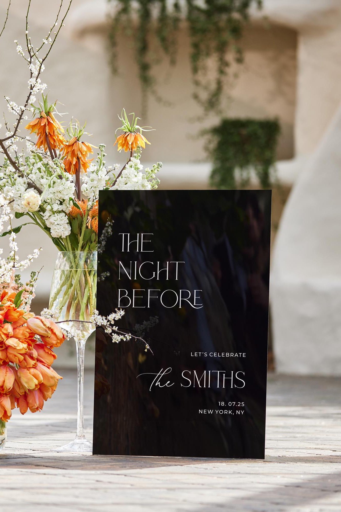 Vertical black acrylic sign styled with floral arrangements for reception entry.