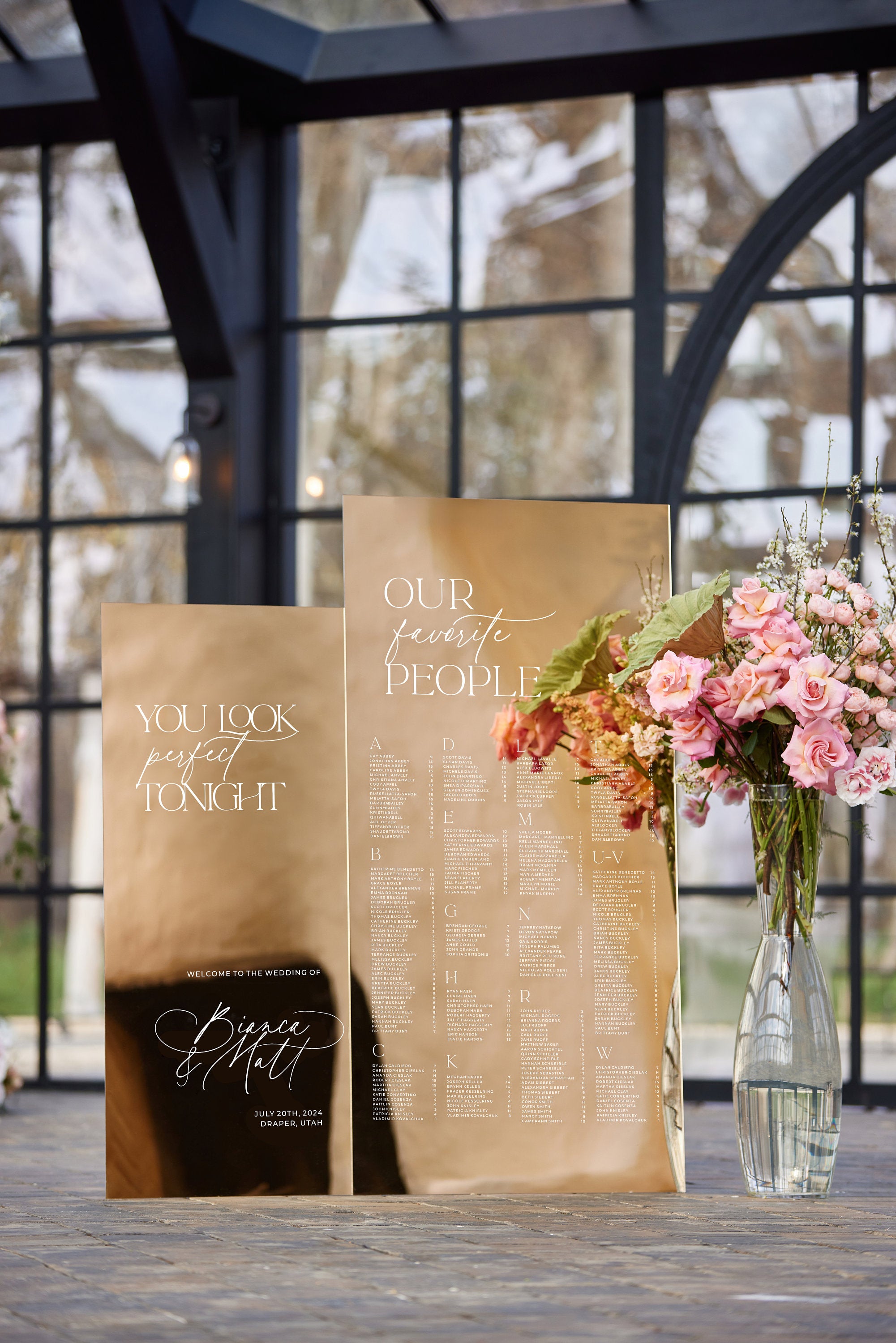 Wedding seating chart in gold mirror acrylic showing personalized guest list and table numbers
