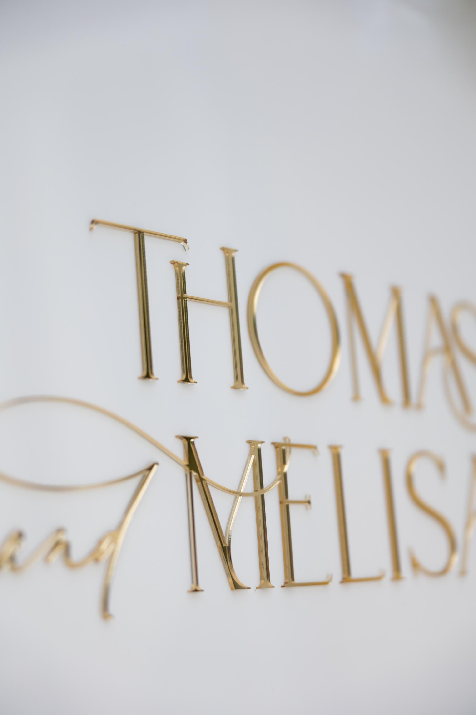 Close-up of 3D gold mirror names on white acrylic wedding welcome sign
