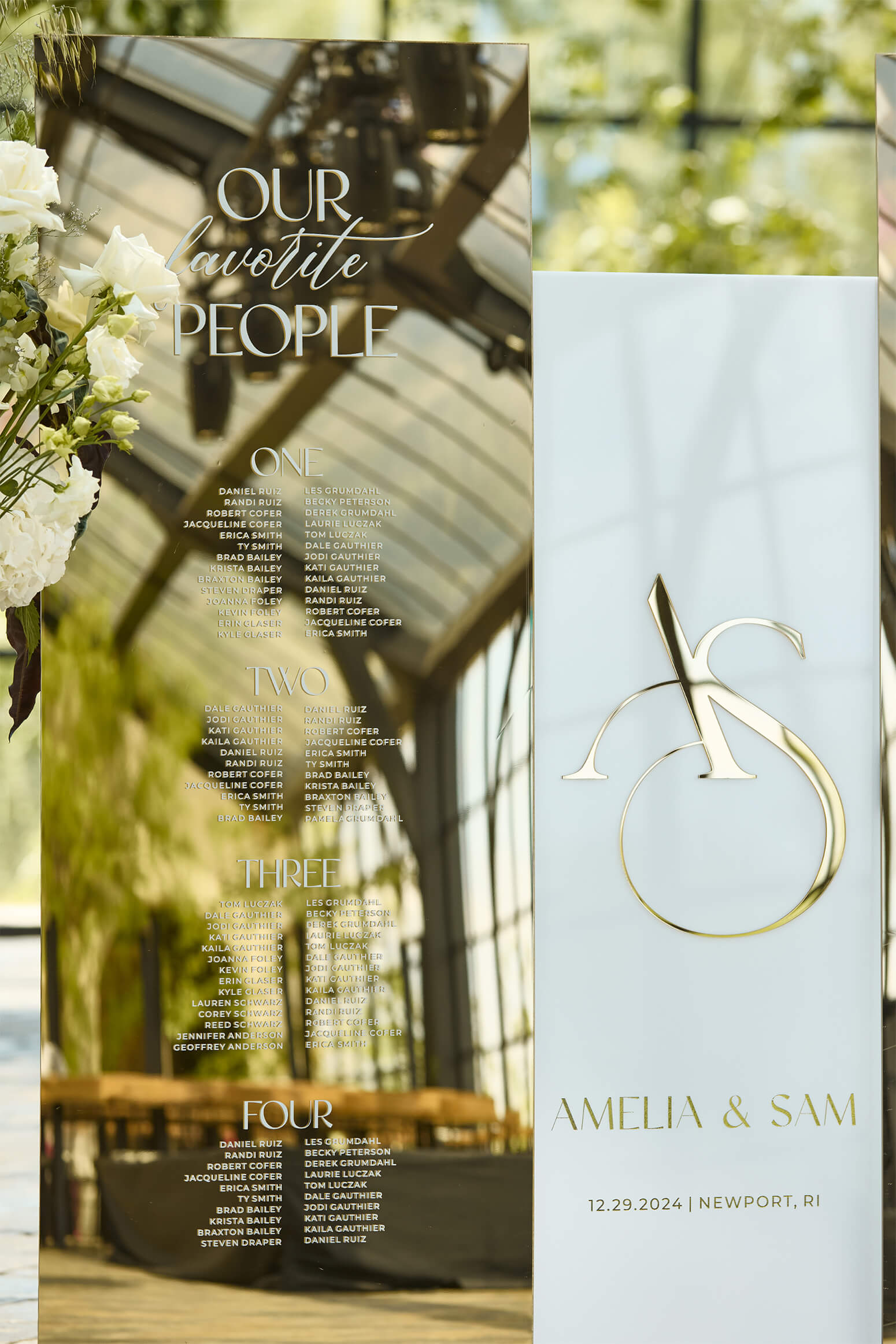 Detail of gold mirror header and guest names arranged by table number on a white acrylic seating chart.