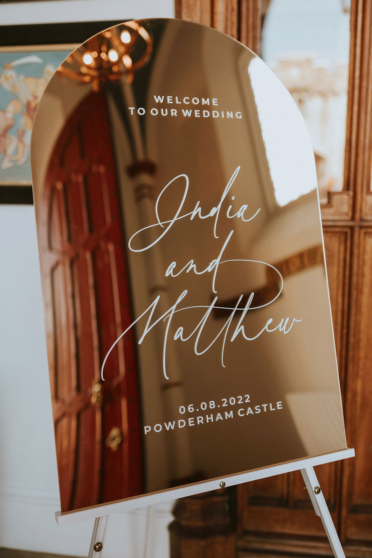 Modern Arched Gold Mirror Sign reflecting the venue interior with white script text.