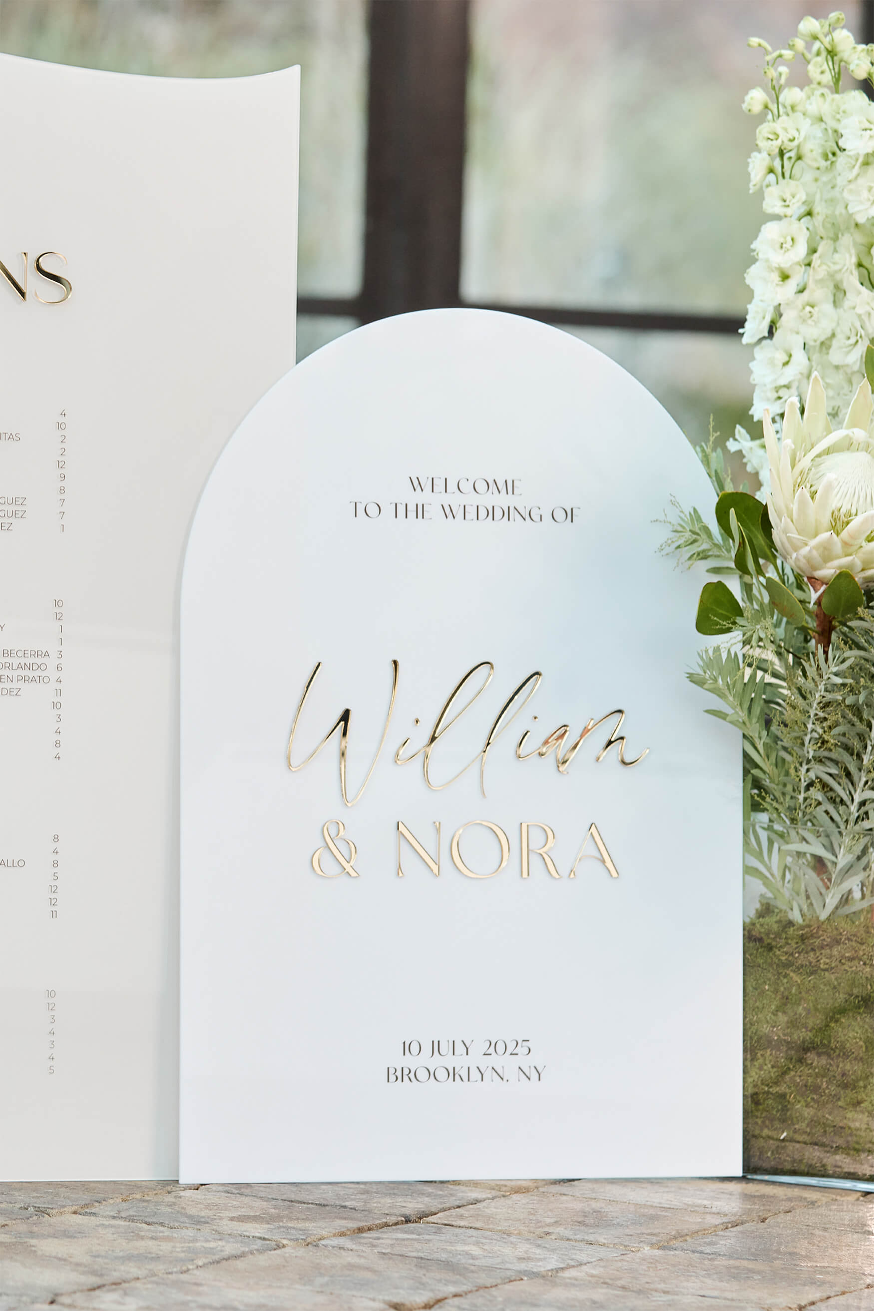 White acrylic wedding welcome sign displaying Bride & Groom names in raised 3D gold mirror.
